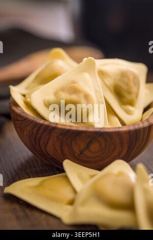 Ravioli triangolari fatti in casa disposti in una ciotola di legno su un tavolo rustico, evidenziando la delicata consistenza della pasta e i centri ripieni. Caldo, confortante Ital Foto Stock
