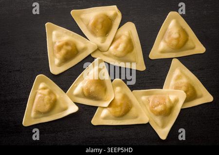 Primo piano di ravioli triangolari su una superficie di legno scuro, evidenziando la pasta ripiena cruda con impasto dorato. Ideale per la cucina italiana, ricetta visua Foto Stock