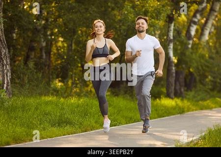 Felice giovane coppia che fa jogging nel parco verde soleggiato e si gode la corsa mattutina e uno stile di vita sano. Foto Stock