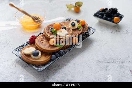 Vista frontale delle mini frittelle dolci ricoperte di frutti di bosco agrumi e miele sul vassoio da portata Foto Stock