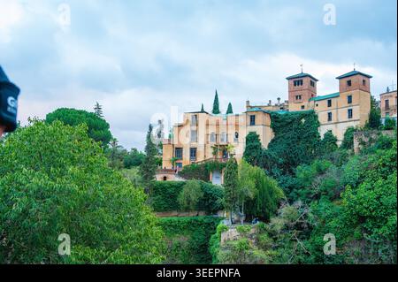 Un edificio storico coperto di edera sorge su una collina verde a Ronda, Andalusia, Spagna. Alberi lussureggianti e vegetazione circondano la struttura in pietra sotto a. Foto Stock