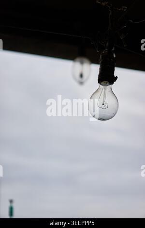 Una lampadina da pesca appesa è in forte risalto sullo sfondo sfocato di un tranquillo porto del Mare dell'Est, con barche ancorate sotto un cielo coperto. Foto Stock