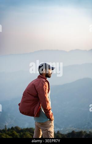 Un uomo barbuto che indossa un berretto e una giacca si affaccia sulle nebbiose catene montuose di Raghupur Fort, Sojha, Manali, Himachal Pradesh, India. Foto Stock