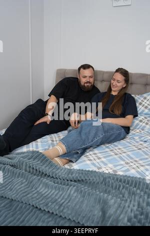 Coppia di adulti che si siede fianco a fianco su un letto tenendosi per mano, condividendo un momento tranquillo e intimo di connessione e comfort in un'accogliente camera da letto di casa Foto Stock