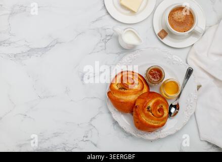 Due panini con uvetta, marmellata e miele in un piatto bianco su sfondo di marmo per la colazione. Caffè, latte, burro sul tavolo. Messa a fuoco selettiva, superiore vi Foto Stock