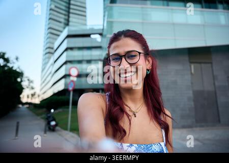 Giovane donna sorridente in un ambiente urbano, godendosi una giornata di sole Foto Stock