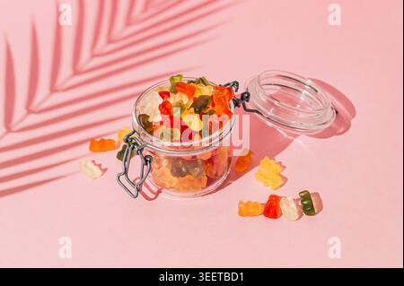 Scena estiva con colorate caramelle gommose e ombra tropicale di foglie di palma su sfondo rosa pastello. Sole e ombre. Il concetto di dolcetti estivi minimal. Foto Stock