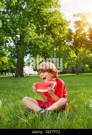 Un bambino felice sorridente in estate con anguria in mano. Succulento rinfresco all'aperto. Foto Stock