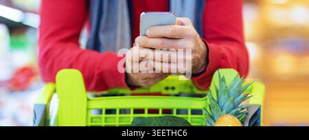 Acquisto di generi alimentari mentre si utilizza uno smartphone in un negozio Foto Stock