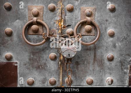Primo piano dello sportello in ferro con anelli arrugginiti, catena pesante e lucchetto vintage Foto Stock