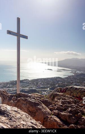 Croce bianca sulla cima della montagna che si affaccia sulla città costiera mediterranea e sul porto. Foto Stock