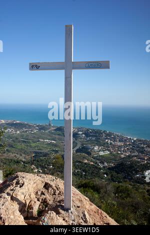 Croce bianca sulla cima della montagna che si affaccia sulla costa mediterranea e sul mare blu. Foto Stock