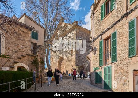 Maiorca, Spagna - 12 maggio 2026: I turisti camminano attraverso una pittoresca strada acciottolata costeggiata da edifici storici in pietra e persiane verdi nel me Foto Stock