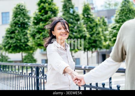 Primo piano ritratto di una donna asiatica sorridente che si tiene per mano con il suo partner sul ponte cittadino Foto Stock