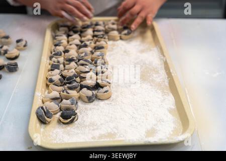 Batuffoli ripieni a forma di mani su vassoio, primo piano di Pasticceria che pizzica piccoli impasti pieni di pasta di sesamo nero su cottura molto infarinata Foto Stock