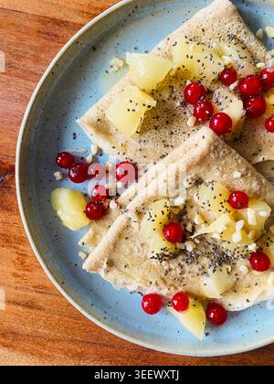 Vista dall'alto di salutari crepes d'avena fatte in casa ricoperte da pezzi di kiwi freschi, melograno e semi di chia su un piatto di ceramica blu. Foto Stock
