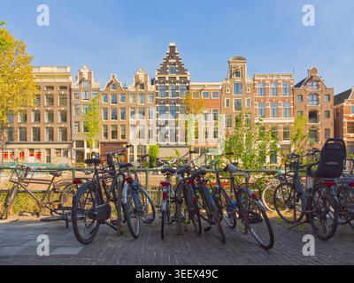 Le tradizionali case olandesi sui canali e le biciclette parcheggiate lungo il canale navigabile di Amsterdam nelle giornate di sole Foto Stock