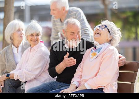 Amici anziani che chiacchierano insieme mentre due di loro flirtavano Foto Stock