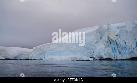 Inquadratura ampia fissa di antichi ghiacciai e montagne coperte di neve che si innalzano su iceberg piatti nelle acque calme della baia Paradise, in Antartide Foto Stock