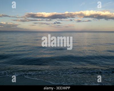 Un mare sereno e tranquillo al tramonto con le onde dolci che scivolano sulla spiaggia sabbiosa sotto un calmo cielo serale. Foto Stock