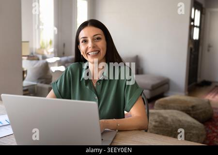 Ritratto di donna che lavora da remoto seduto a un tavolo con un notebook Foto Stock
