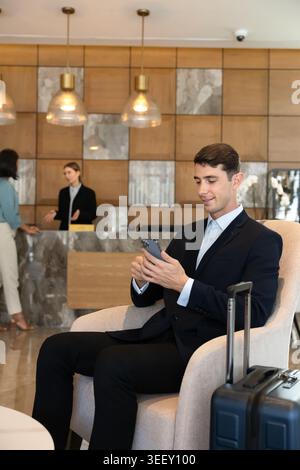 Uomo d'affari seduto nella hall dell'hotel utilizzando lo smartphone Foto Stock