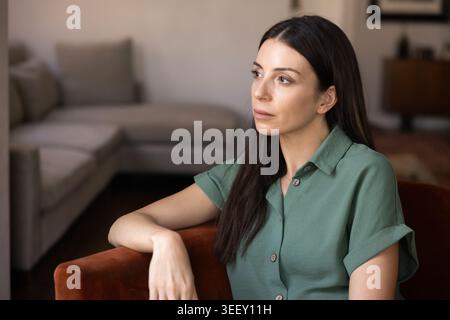 Donna pensiva single seduta su poltrona nel moderno soggiorno Foto Stock