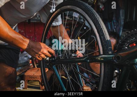 Le mani di un meccanico regolano la ruota posteriore e il deragliatore di una bicicletta. L'immagine acquisisce il lavoro del manuale tecnico. Foto Stock