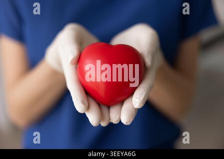 Primo piano dell'operatore sanitario tiene il cuore rosso nelle mani Foto Stock