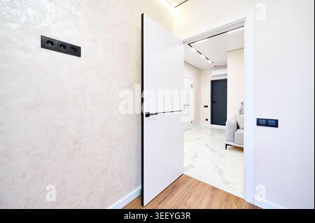 Interni luminosi e non arredati con laminato in legno chiaro, pareti con finitura testurizzata e soffice illuminazione a soffitto. Camera residenziale pulita, proprietà immobiliari e stile di vita moderno Foto Stock
