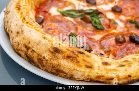 Pizza al peperoni sul piatto del ristorante, Pizza al salame con olive, pomodori e mozzarella, primo piano di pane italiano tradizionale Foto Stock