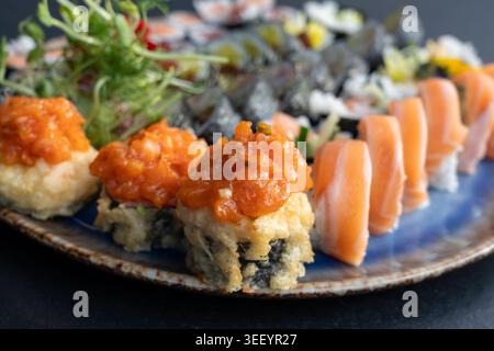 Sushi tempura croccanti ricoperti di salmone piccante, microgreen freschi, dolci assortiti di maki e fiori commestibili su un set di piatti di sushi Foto Stock