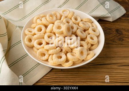 Anelli di cereali su tavolo di legno, anelli di riso per la colazione, snack di cereali di mais su sfondo rustico Foto Stock