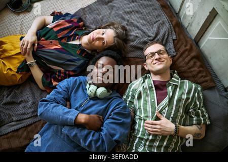 Ritratto di diversi giovani adulti sdraiati insieme e sorridenti alla macchina fotografica, esprimendo amicizia e inclusione. Utile per il marketing della diversità, le campagne della community, la vista dall'alto Foto Stock
