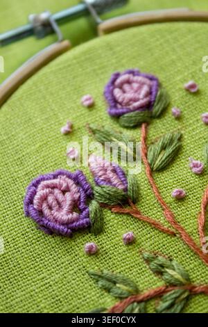 Cerchio da ricamo con ricami floreali fatti a mano su tessuto verde, vista ravvicinata della lavorazione a ago e della consistenza tessile. Tradizionale concetto di hobby fai da te Foto Stock