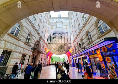 La gente cammina sotto una grande scultura lunare nelle strade della città di Budapest. La scultura crea una vista unica nell'area urbana. Foto Stock