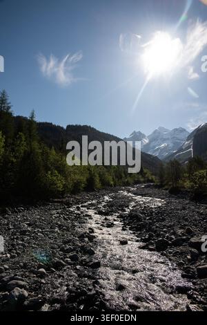 Valle alpina illuminata dal sole con un ruscello roccioso che conduce a vette innevate - zona Oeschinensee, Kandersteg, Cantone di Berna, Svizzera Foto Stock