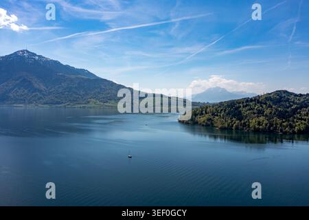 Vista aerea sul tranquillo litorale del lago Zug - barca a vela su acque blu profonde con vette alpine e cielo limpido Foto Stock