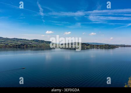 Vista panoramica sul litorale del lago Zug e sulle colline ondulate - acque blu tranquille con piccola barca e increspature Foto Stock