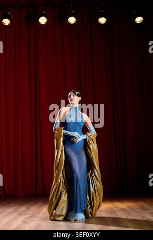 Una bella donna si erge graziosamente sul palco, drappeggiata in un tessuto elegante che irradia fascino artistico. Foto Stock