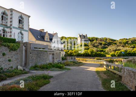 Vista delle case costiere sopra la spiaggia di Portez le Conquet Finistere Bretagna Francia che mostra muri in pietra, sentiero, vegetazione verde e tradizionale arco costiero Foto Stock