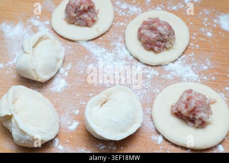 Gnocchi con carne. Il processo di cottura dei gyoza asiatici. Farina, impasto su sfondo wodden. Gnocchi, impasto e carne macinata fatti in casa Foto Stock