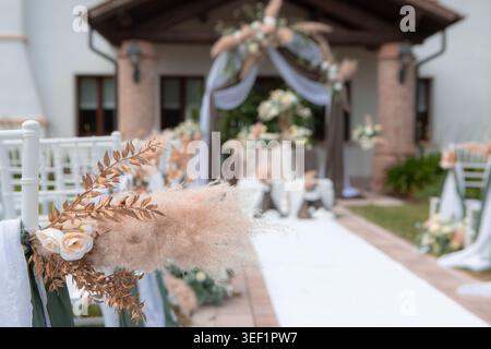Sala per cerimonie nuziali con eleganti sedie bianche e un arco floreale con erba di pampas Foto Stock