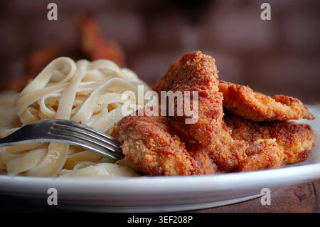Pollo impanato, pesce, gamberi o cotolette di manzo, con tagliatelle o fettuccine e forchetta laterale, vista laterale con cotolette impanate sullo sfondo Foto Stock