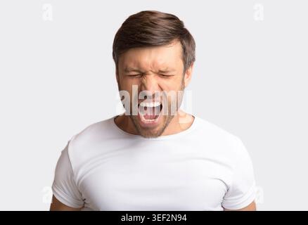 Ritratto di Emotional Man urlando furiosamente su sfondo bianco Foto Stock