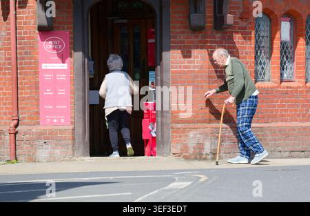 Anziano anziano che cammina con un bastone come aiuto per camminare, nei negozi di una città, in una giornata di sole primaverili in Inghilterra, Regno Unito. Foto Stock