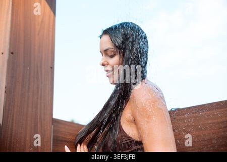 Ritratto di una modella donna che posa sotto il flusso d'acqua all'aperto. Giovane donna che rinfresca la pelle accanto a una destinazione di vacanza tropicale. Concetto di stile Spa. Foto Stock