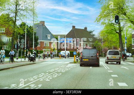 Amsterdam, Paesi Bassi - 17 aprile 2026: Un incrocio urbano in una zona residenziale con ciclisti, semafori e cartelli direzionali blu Foto Stock
