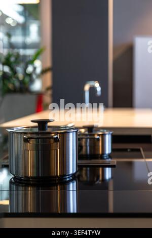 Pentola in acciaio inox su piano cottura a induzione nero. Cucina dal design moderno. Foto Stock