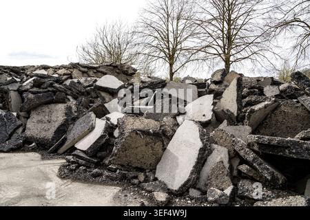 Vecchi pezzi di asfalto provenienti da cantieri stradali, accatastati per il riutilizzo o lo smaltimento in una discarica di rifiuti pericolosi Foto Stock
